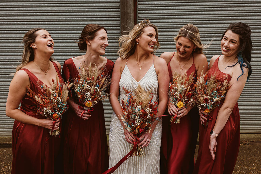 Bride and bridesmaids in red dresses holding dried flower bouquets from Hidden Botanics.