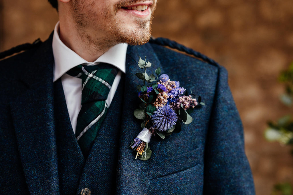 Groom wears Hidden Botanics purple dried flowers buttonhole for wedding.