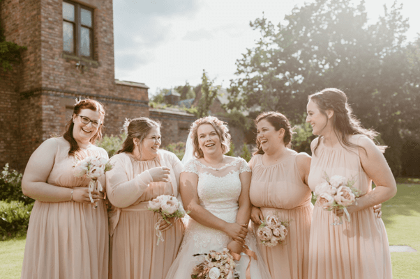 A Bride with her bridesmaids holding round-shaped bouquets from Hidden Botanics outside in a garden.