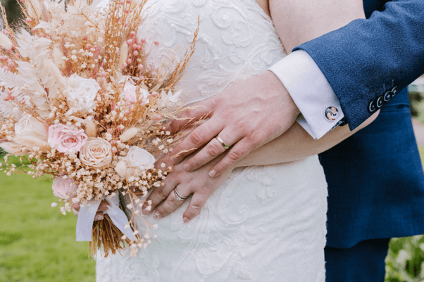 A bride and groom hugging with a wedding bouquet of dried and fresh flowers.